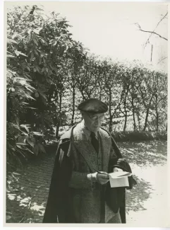 photographie d’André Gide, avec lunettes et béret, debout, prenant des notes, en extérieur, 3 avril 1947