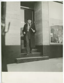 photographie d'André Gide, avec lunettes et béret, descendant l'escalier d'un commerce