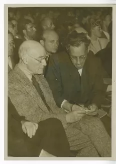 photographie d’André Gide, avec lunettes, et Jef Last, assis parmi le public d'une conférence, juin 1947