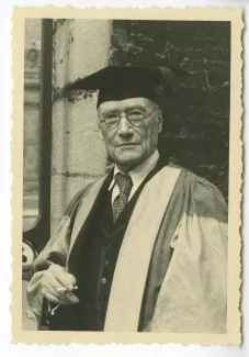 portrait photographique en buste d’André Gide, en costume de docteur Honoris Causa de l'Université d'Oxford, devant un portail, 7 juin 1947