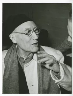photographie en gros plan d’André Gide, avec lunettes et bonnet, souriant à Pierre Herbart, au Vaneau, février 1950 ; reportage pour Paris-Match