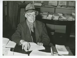 portrait photographique en buste d’André Gide, avec lunettes et chapeau, assis à un bureau, au Vaneau, février 1950 ; reportage pour Paris-Match