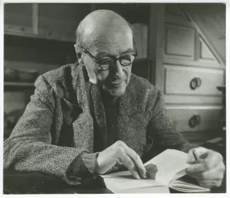 portrait photographique en buste d’André Gide, avec lunettes, attablé, lisant un livre, au Vaneau, lors du tournage du film Avec André Gide de Marc Allégret, janvier 1951 ; reportage pour Paris-Match