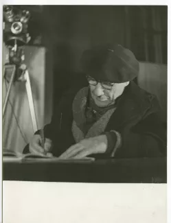 portrait photographique en buste d’André Gide, avec lunettes et béret, attablé, écrivant, au Vaneau, lors du tournage du film Avec André Gide de Marc Allégret, janvier 1951 ; reportage pour Paris-Match