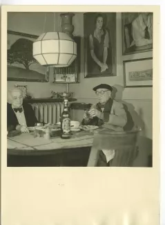 photographie d’André Gide, avec lunettes et béret, et Maria Van Rysselberghe, dans l'appartement de Maria, simulant un déjeuner, lors du tournage du film Avec André Gide de Marc Allégret, janvier 1951