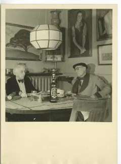 photographie d’André Gide, avec lunettes et béret, et Maria Van Rysselberghe, dans l'appartement de Maria, simulant un déjeuner, lors du tournage du film Avec André Gide de Marc Allégret, janvier 1951