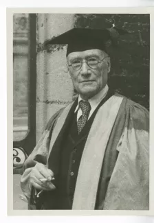 portrait photographique en buste d’André Gide, en costume de docteur Honoris Causa de l'Université d'Oxford, devant un portail, 7 juin 1947