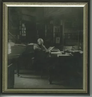 portrait photographique d’André Gide, avec lunettes, assis à son bureau, regardant une grande image, au Vaneau