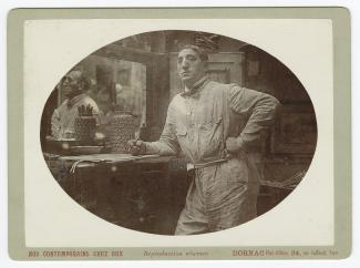 portrait photographique de Théo Van Rysselberghe, accoudé à une commode, en tenue de travail, dans son atelier de la villa Aublet, rue Laugier