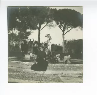 photographie de Maria Van Rysselberghe, assise devant la fontaine de l'esplanade dans le jardin de la villa Médicis, avec la statue colossale de la déesse Rome en arrière-plan, février-mars 1909