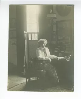portrait photographique de Maria Van Rysselberghe, assise à un secrétaire, avec au mur un portrait dessiné d'Émile Verhaeren par Théo Van Rysselberghe (1892), à la villa Aublet, rue Laugier