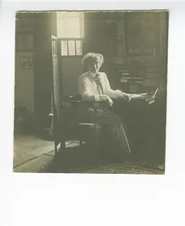 portrait photographique de Maria Van Rysselberghe, assise à un secrétaire, avec au mur un portrait dessiné d'Émile Verhaeren par Théo Van Rysselberghe (1892), à la villa Aublet, rue Laugier