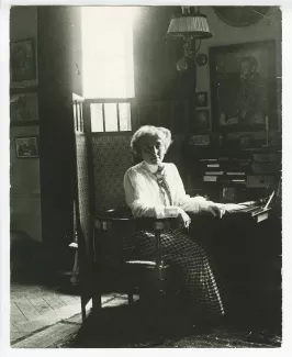 portrait photographique de Maria Van Rysselberghe, assise à un secrétaire, avec au mur un portrait dessiné d'Émile Verhaeren par Théo Van Rysselberghe (1892), à la villa Aublet, rue Laugier