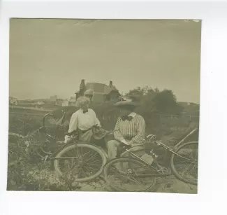 photographie de Maria Van Rysselberghe, à gauche, et Laure Flé, assises dans l'herbe devant leurs vélos, août 1909