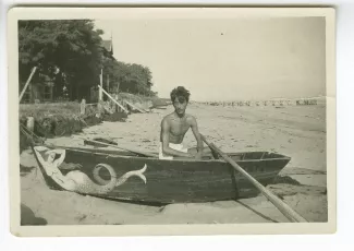 photographie de Jean Cocteau, torse nu, dans une barque sur une plage