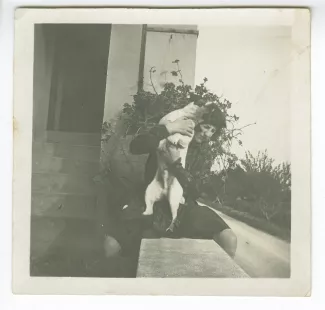 photographie d'Andrée Mayrisch enfant, aux cheveux longs, assise, avec le chien Nick, à l'entrée de la villa de Saint-Clair