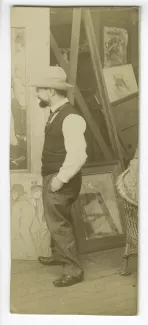 photographie d'Henri de Toulouse-Lautrec, dans son atelier, devant Au salon de la rue des Moulins (1894) accroché au mur, à ses pieds à gauche, Alfred la Guigne (1894), et à droite, sous verre, La Femme aux gants (1890)