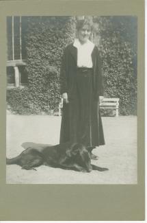 portrait photographique en pied de Suzanne Schlumberger, un chien couché à ses pieds, devant la propriété de ses parents, le château de Bois-Salair