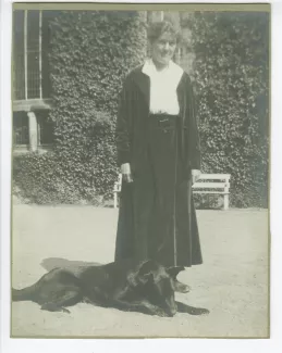 portrait photographique en pied de Suzanne Schlumberger, un chien couché à ses pieds, devant la propriété de ses parents, le château de Bois-Salair