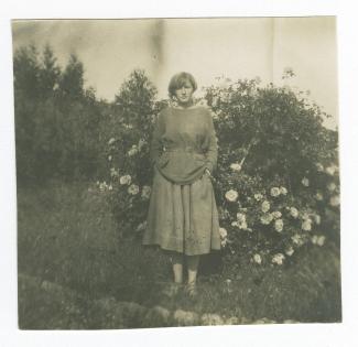 portrait photographique en pied de Monique Schlumberger debout devant un rosier, dans le jardin de la villa de Saint-Clair